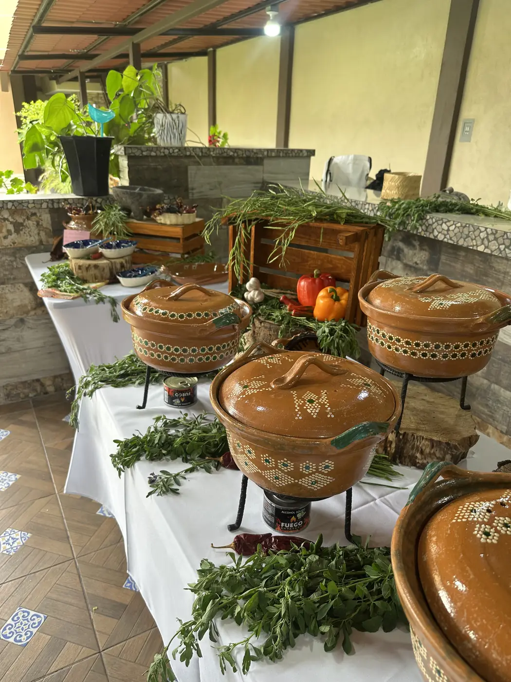 Cazuelas de barro sobre sus anafres, con hierbas y chiles en la mesa